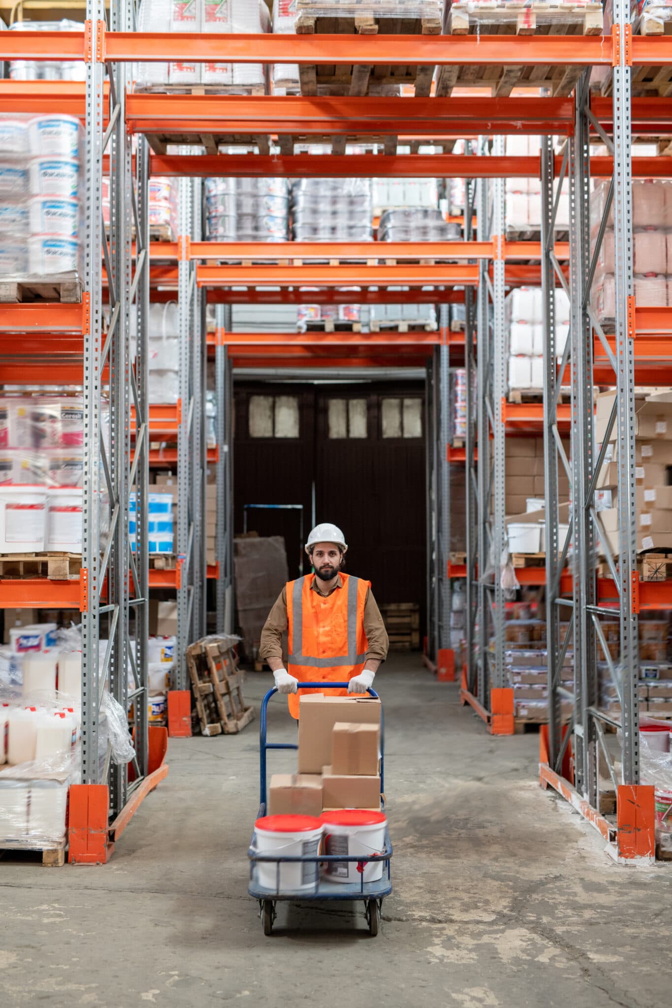 Warehouse worker pushing a trolley of goods between stocked pallet racks