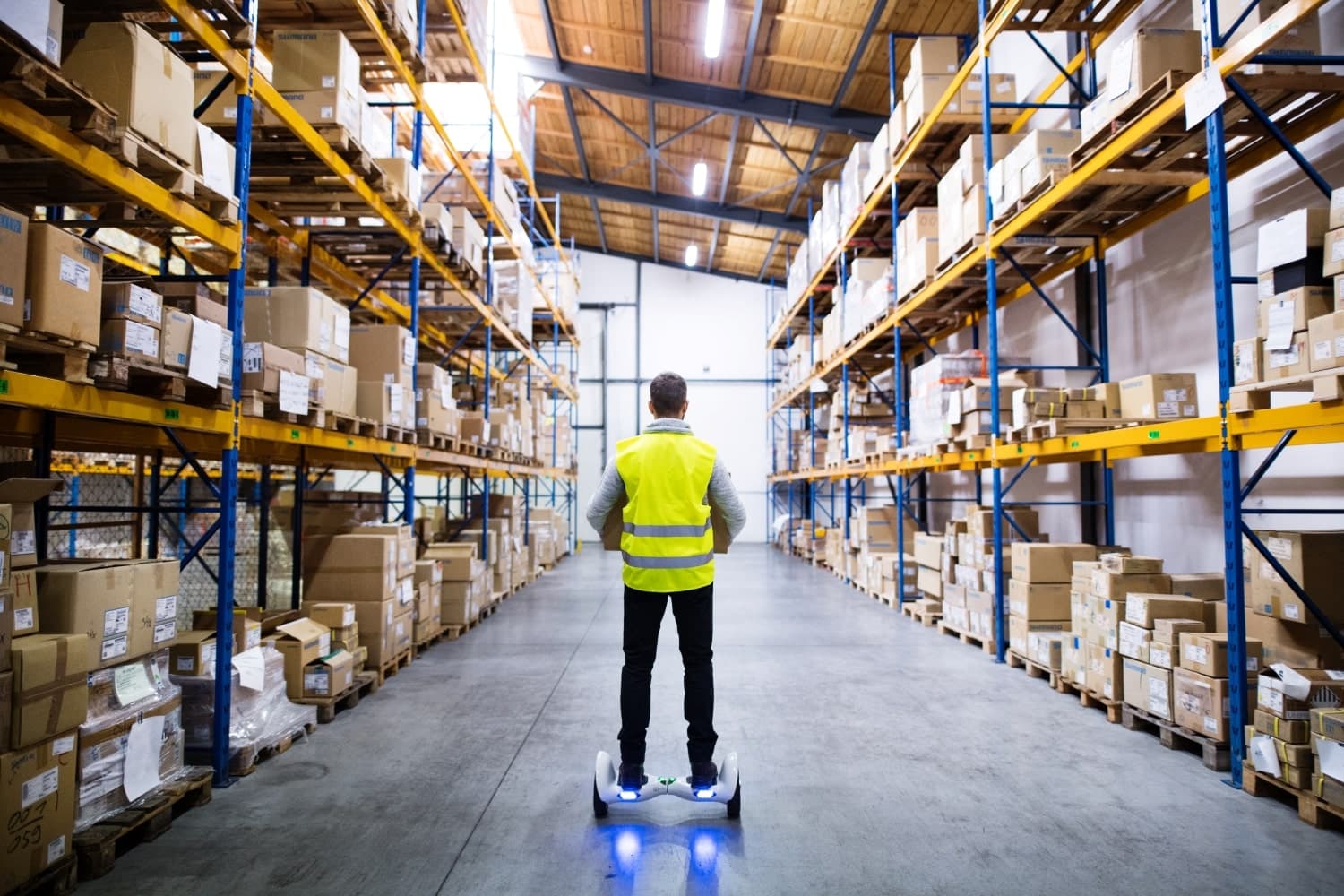 Warehouse worker in a high-visibility vest between shelves of boxed inventory