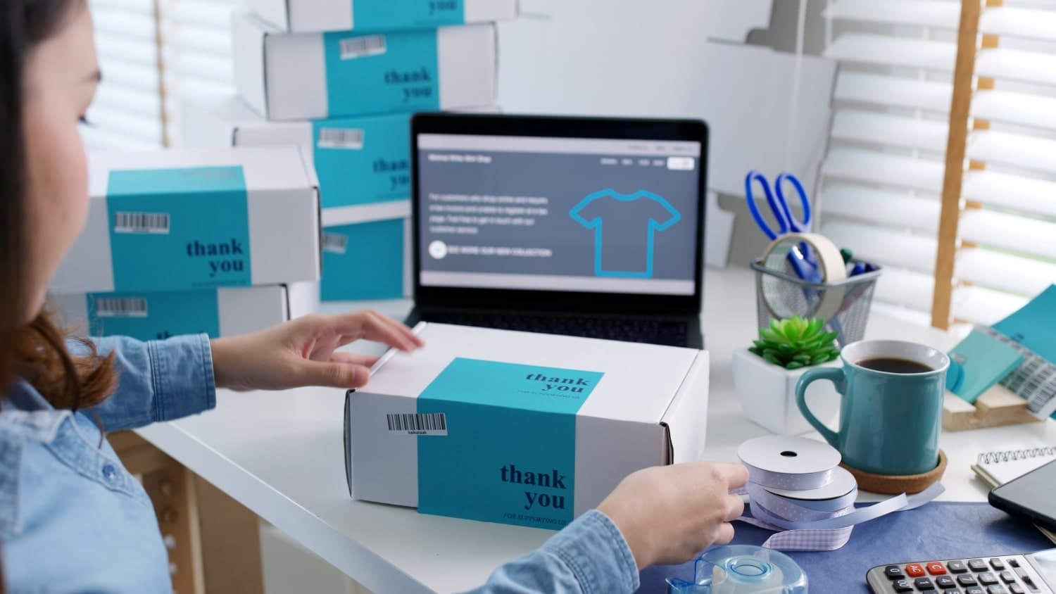 Worker preparing a branded parcel beside a laptop and packing supplies